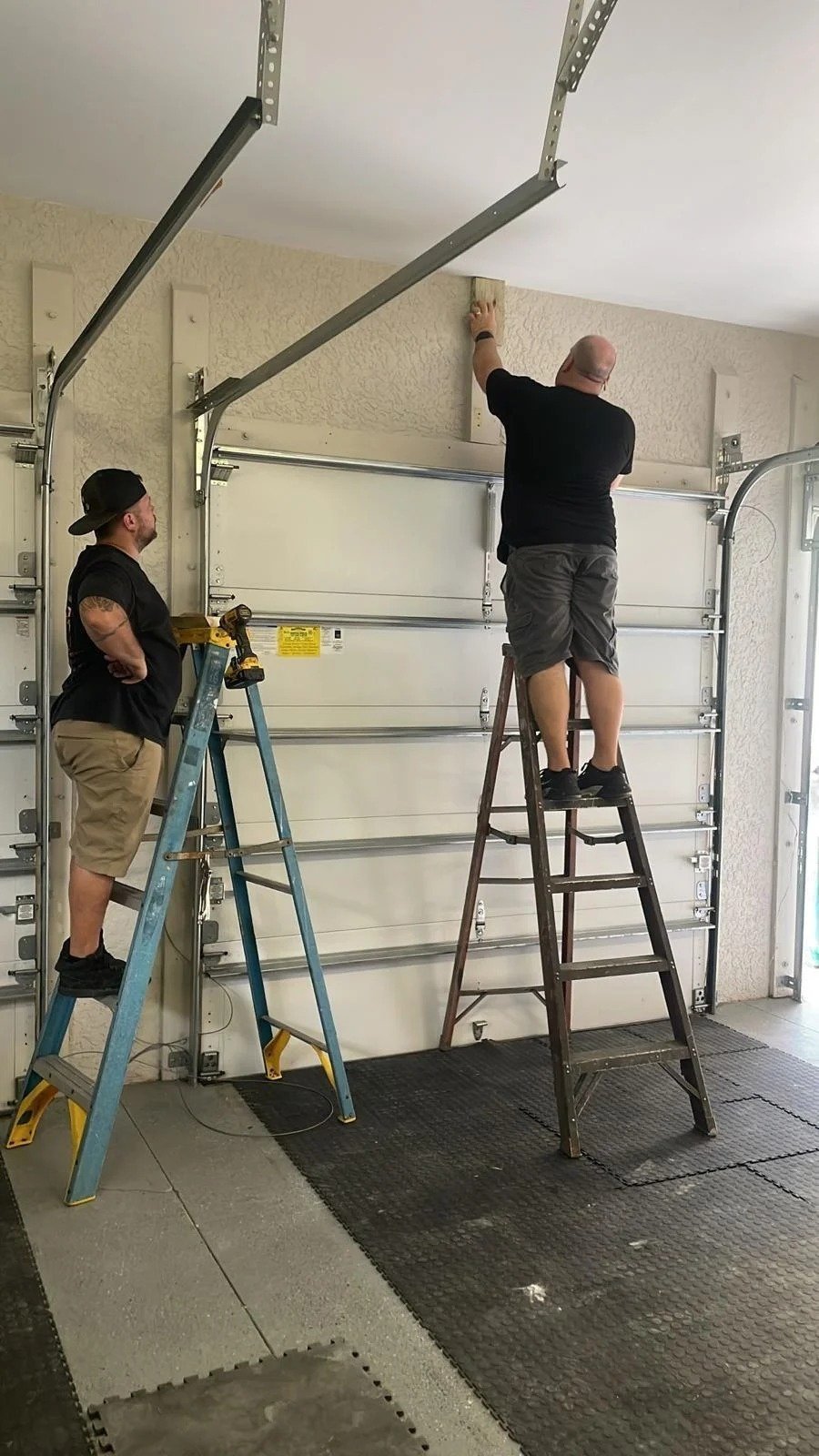 Two people on ladders near overhead door hardware