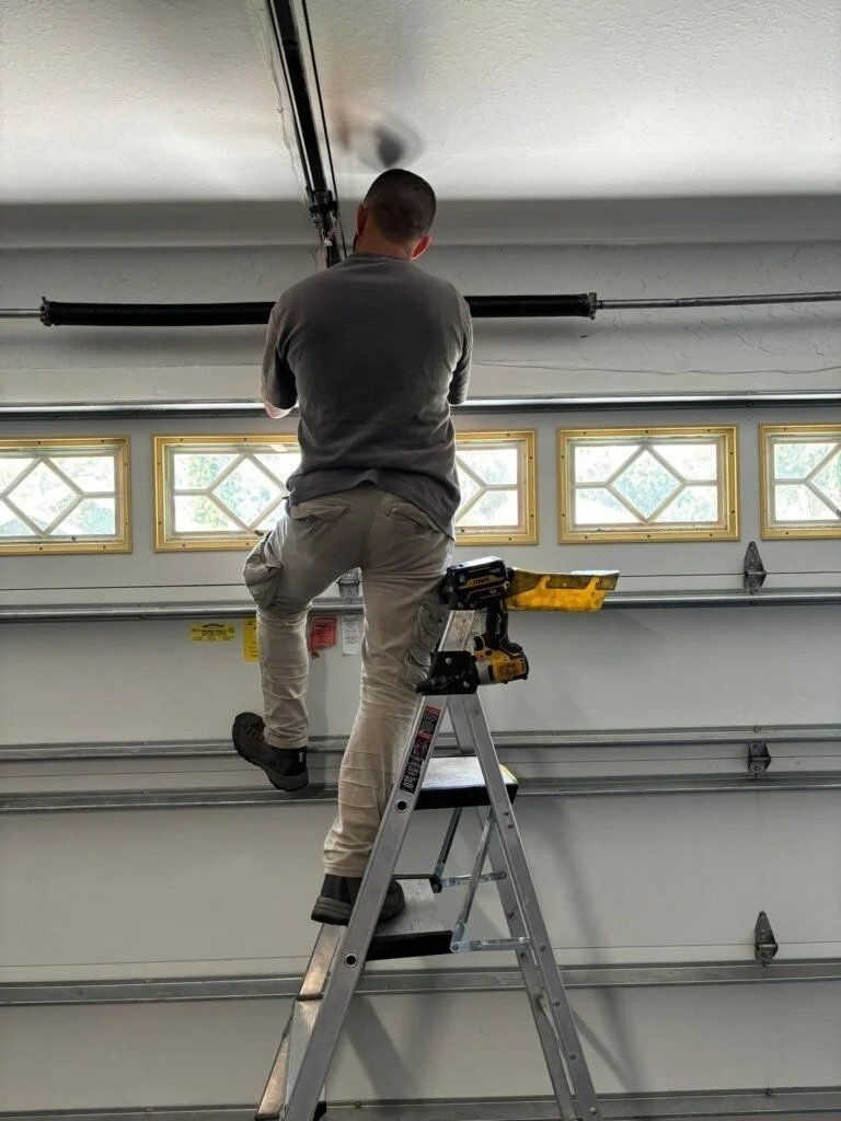 A person on a ladder beside the top section of a garage door