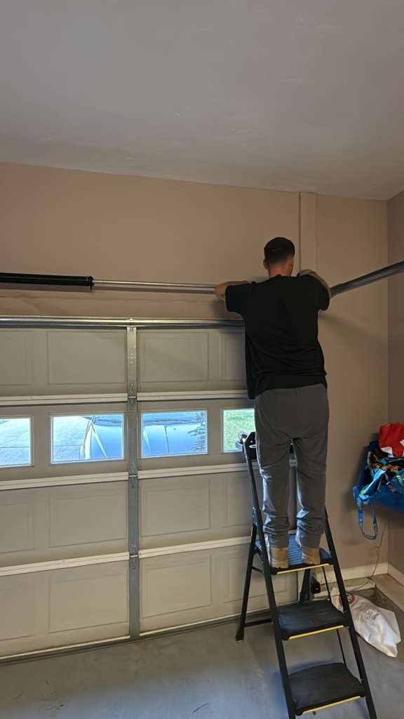 A person on a ladder at the upper corner of a garage door
